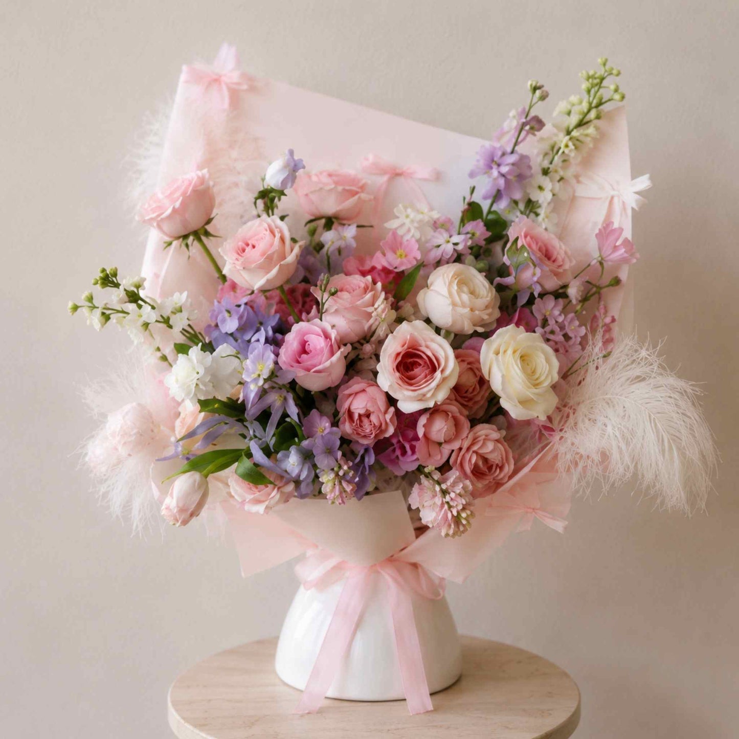 Bouquet of pink and white flowers with a white vase on a wooden stand against a beige background