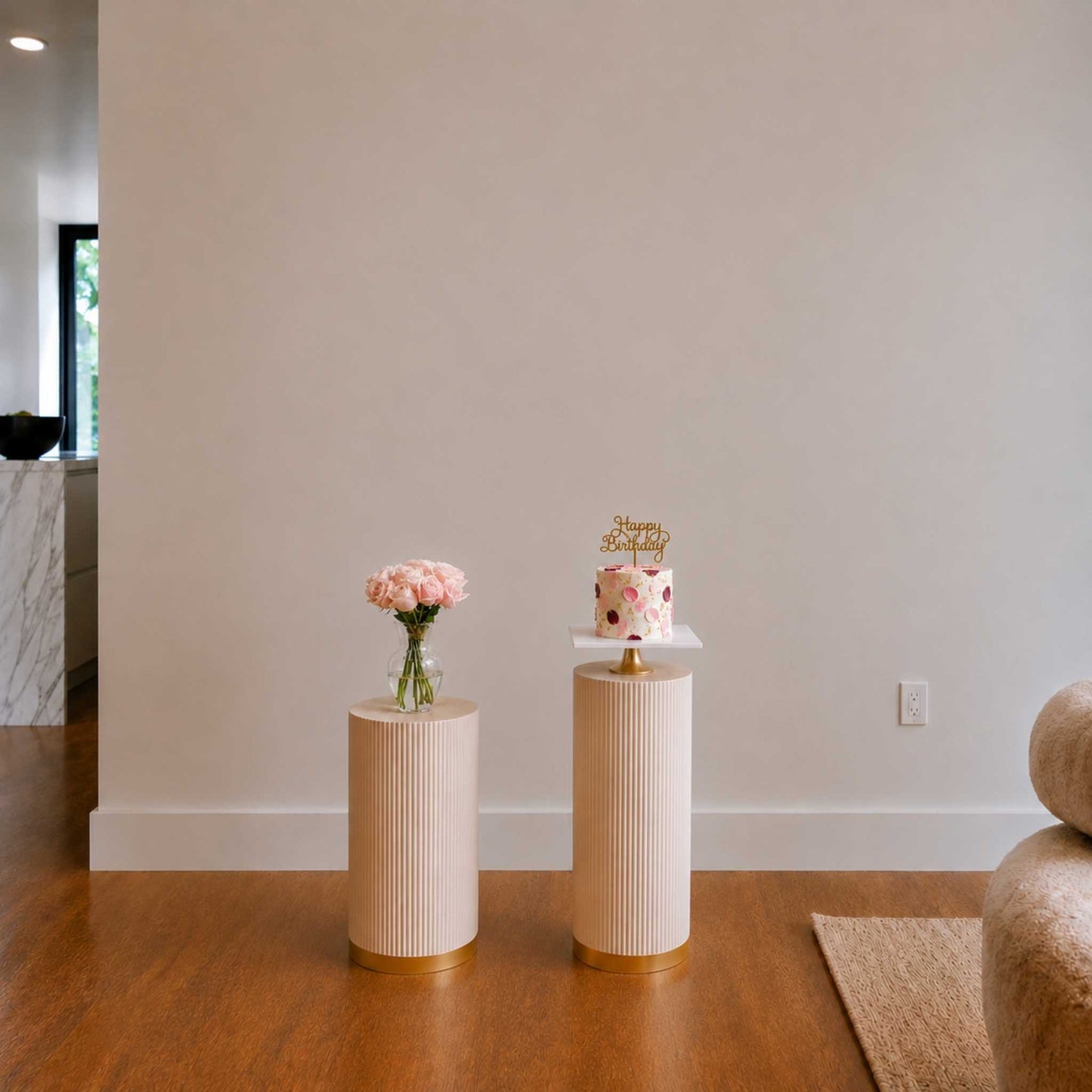 Two small round tables with a cake and flowers against a white wall.