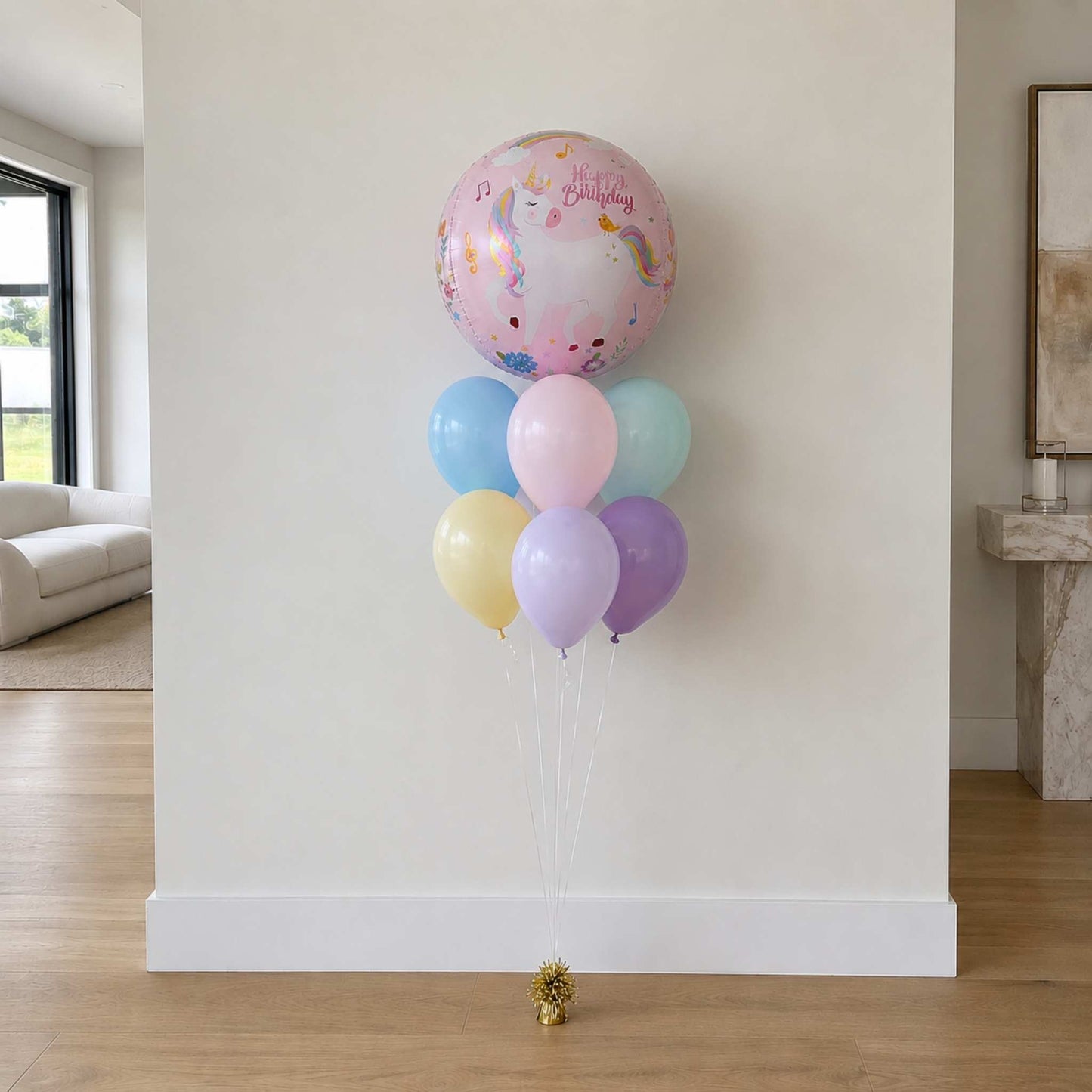 Pastel-colored balloons against a white wall in a room with a couch and window.