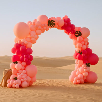 Balloon arch in pink and red colors with leaf decorations against a desert backdrop