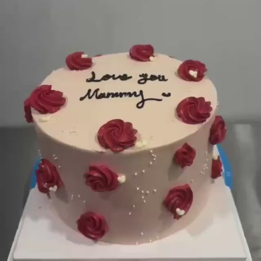 Love you mommy cake staged on table white outside with red roses and small crystals, black text eatable.  