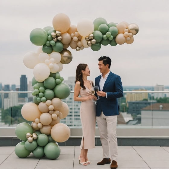 man and woman standing in front of a luxury balloon garland on a roof top with drinks 