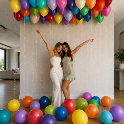 Two women posing with colorful balloons inside a home.