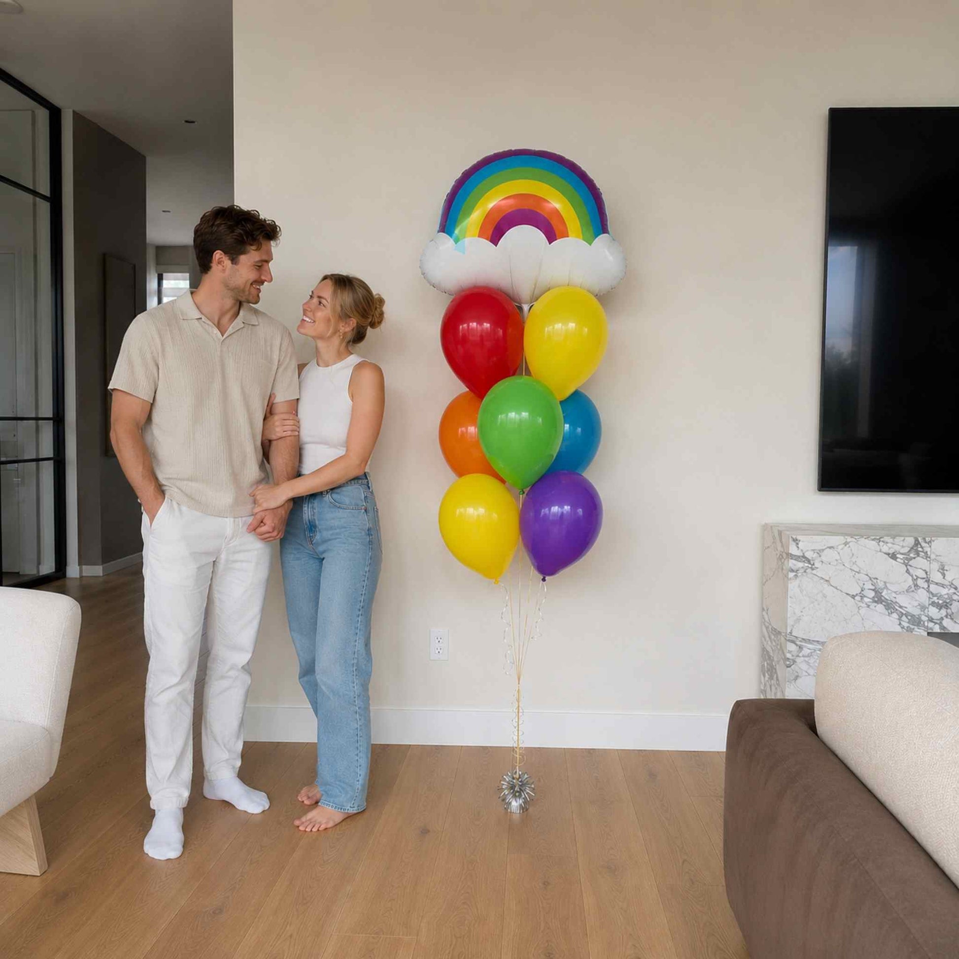 Man and woman standing in a living room with colorful balloons shaped like a rainbow and hearts.
