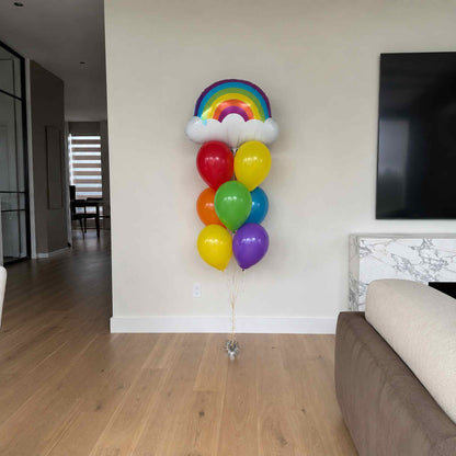 Colorful balloons shaped like a rainbow on a wooden floor in a living room.