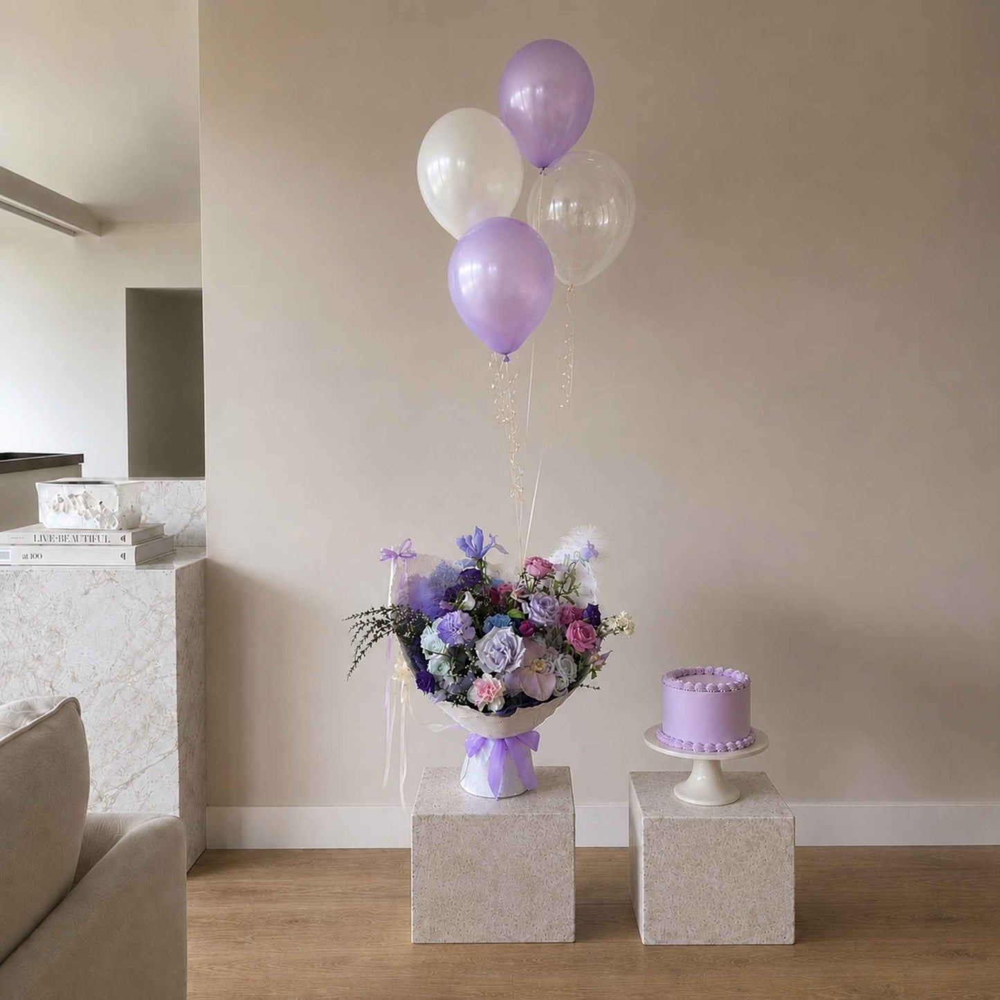 Bouquet of flowers and purple balloons on a stand with a small cake in a room.