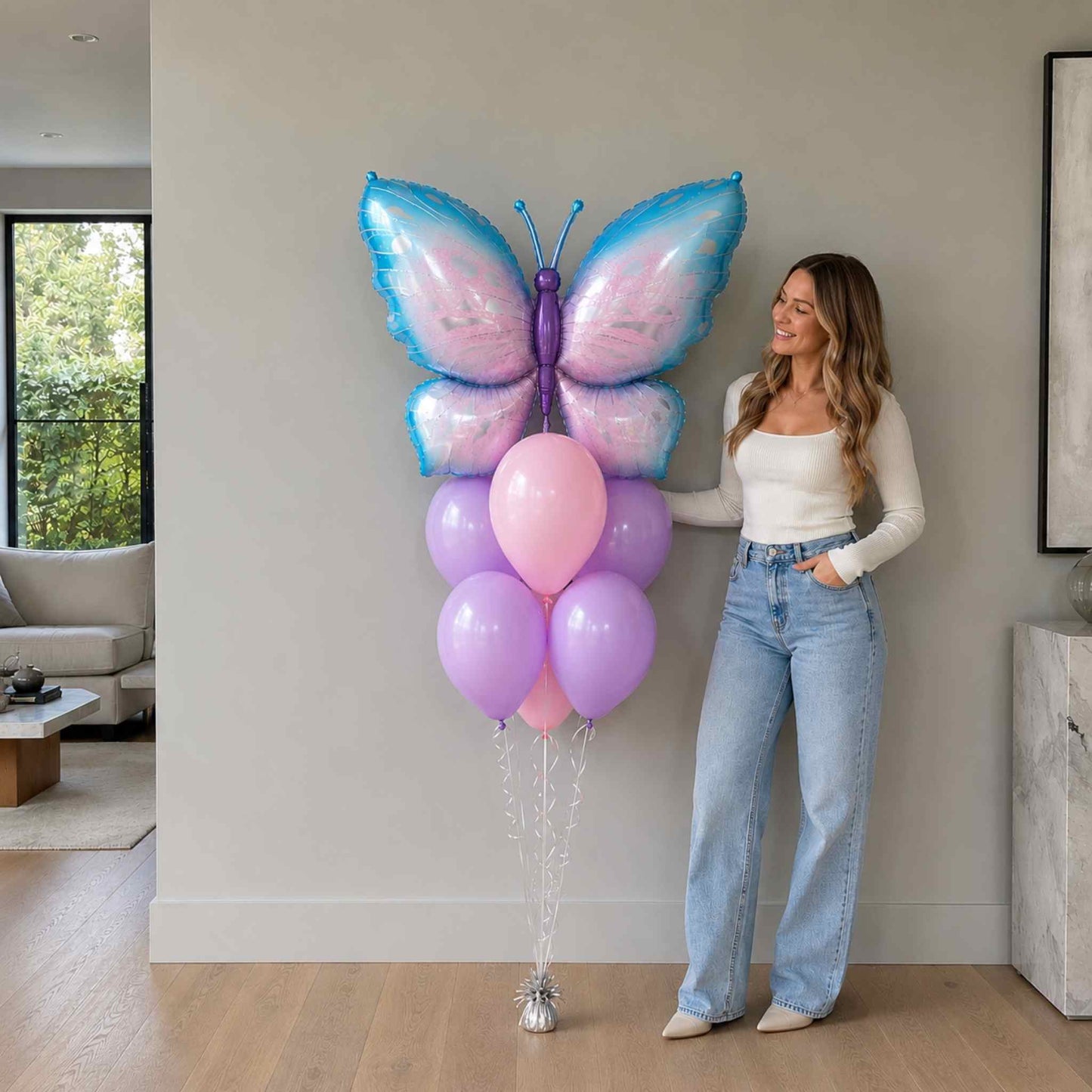 Woman holding a large butterfly-shaped balloon with pink and purple balloons indoors.