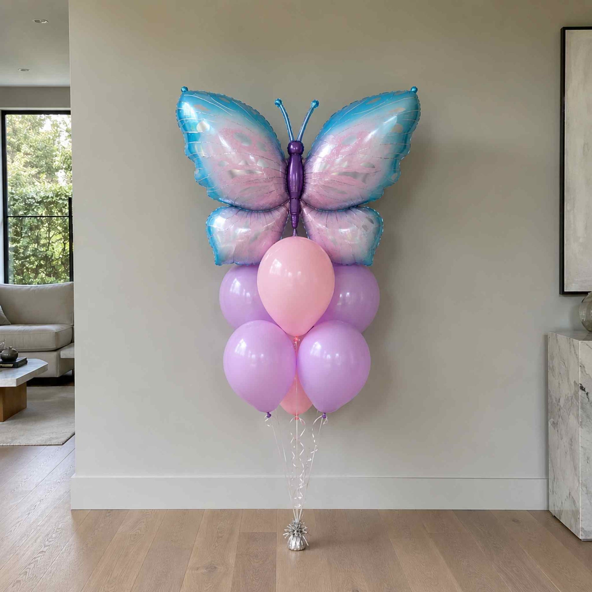 Butterfly-shaped balloon with pink and purple balloons against a neutral wall.