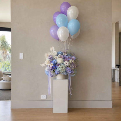 Floral arrangement with balloons on a pedestal in a room.