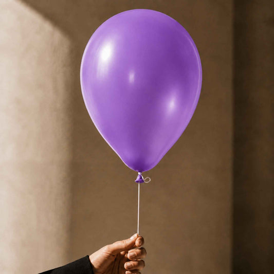 A single matte purple balloon held by a hand against a warm beige wall.