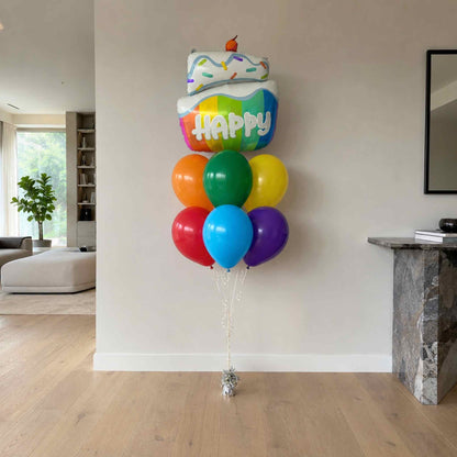 Colorful balloons with a cake-shaped balloon labeled 'Happy' in a living room.