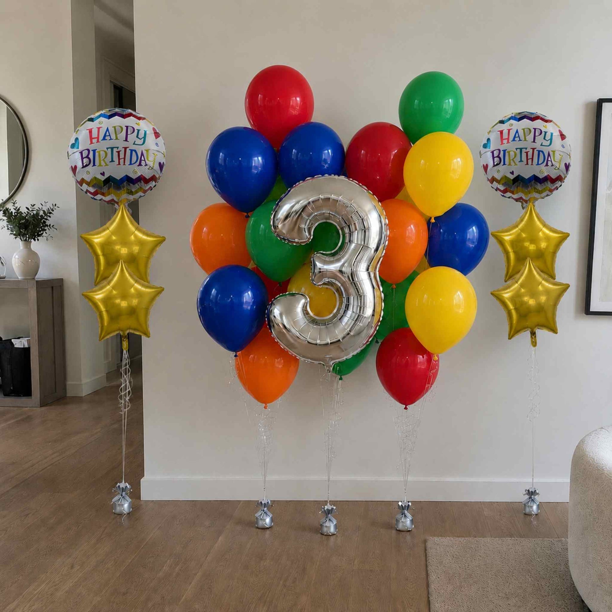 Colorful birthday balloons with a large silver number '3' in a living room setting.