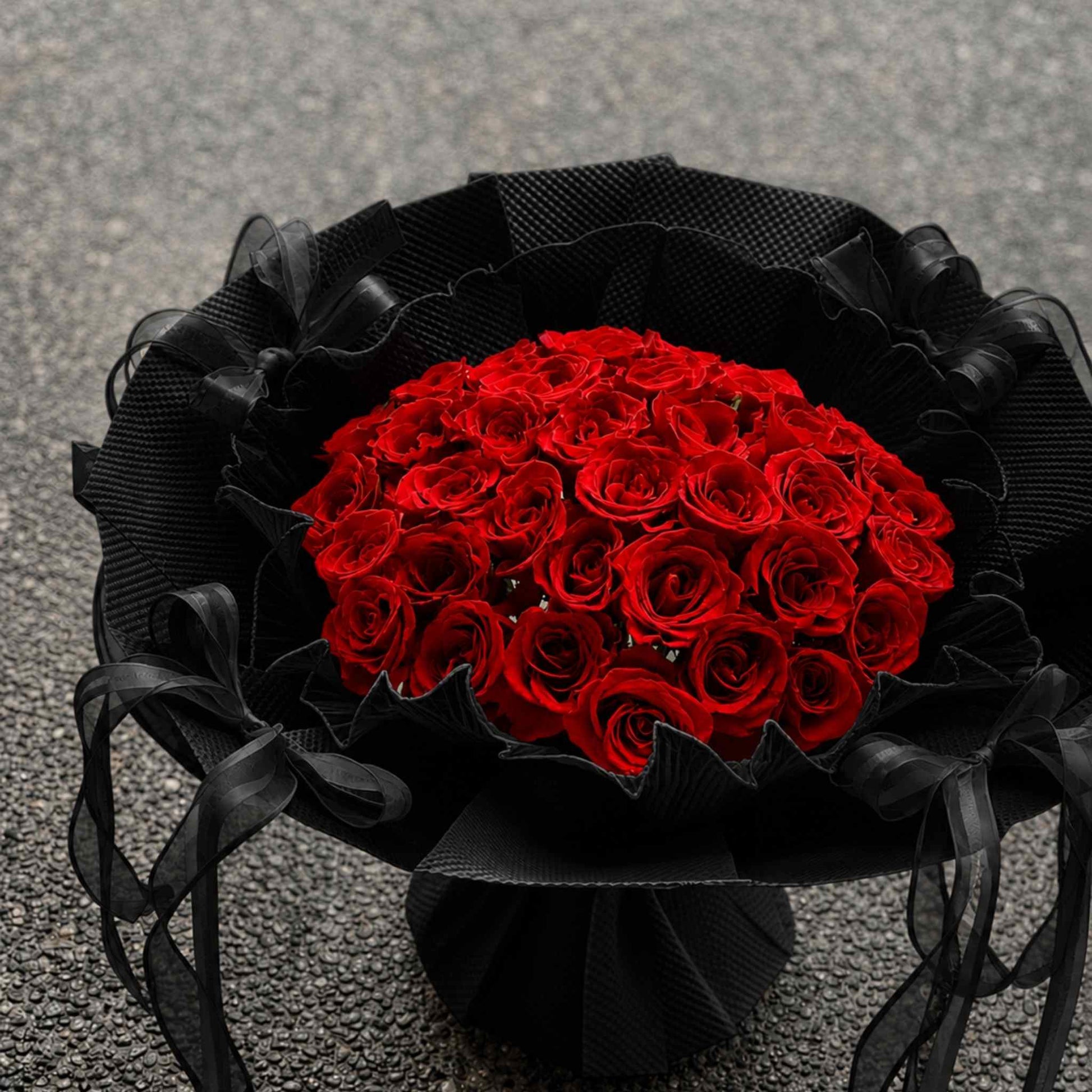 Bouquet of red roses wrapped in black ribbon on a gray background