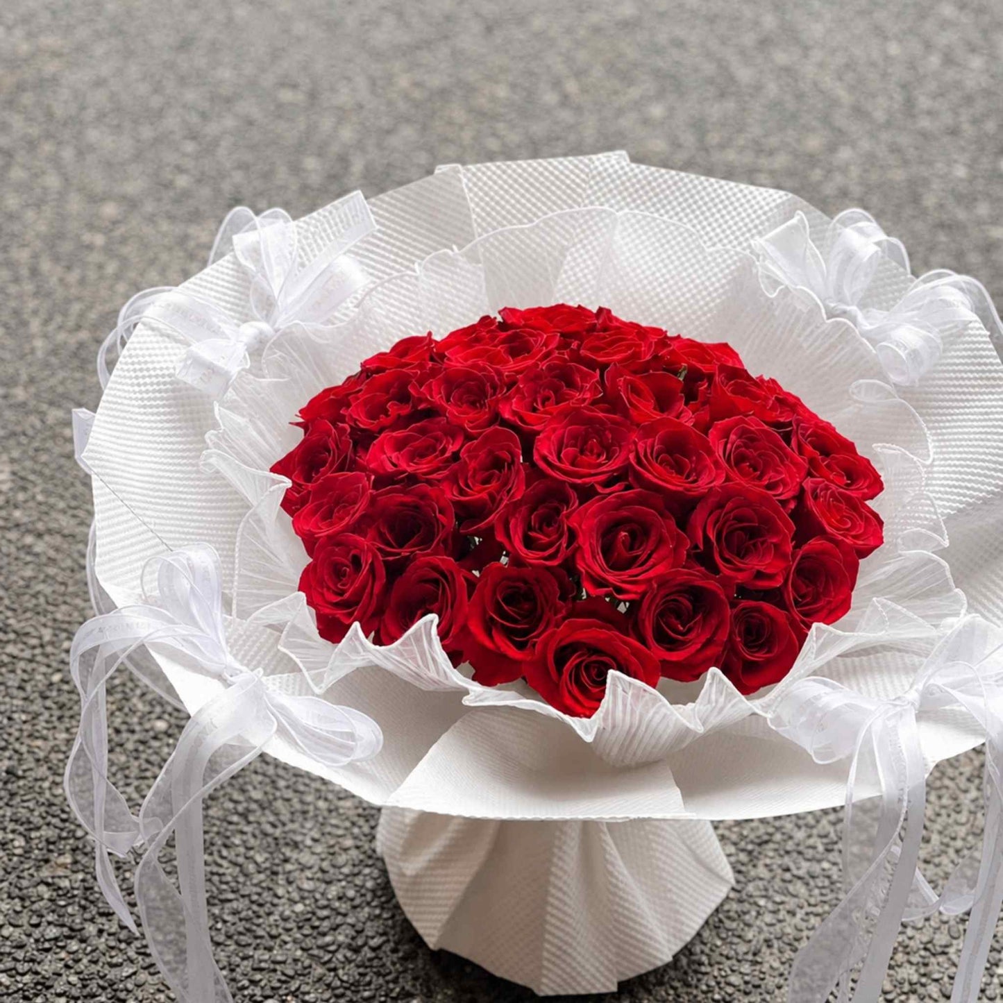 Bouquet of red roses wrapped in white paper and ribbons on a gray surface