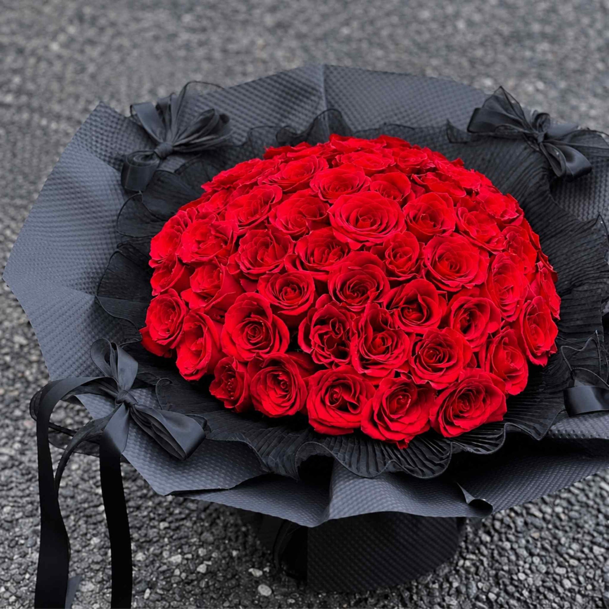 Bouquet of red roses wrapped in black paper on a textured surface