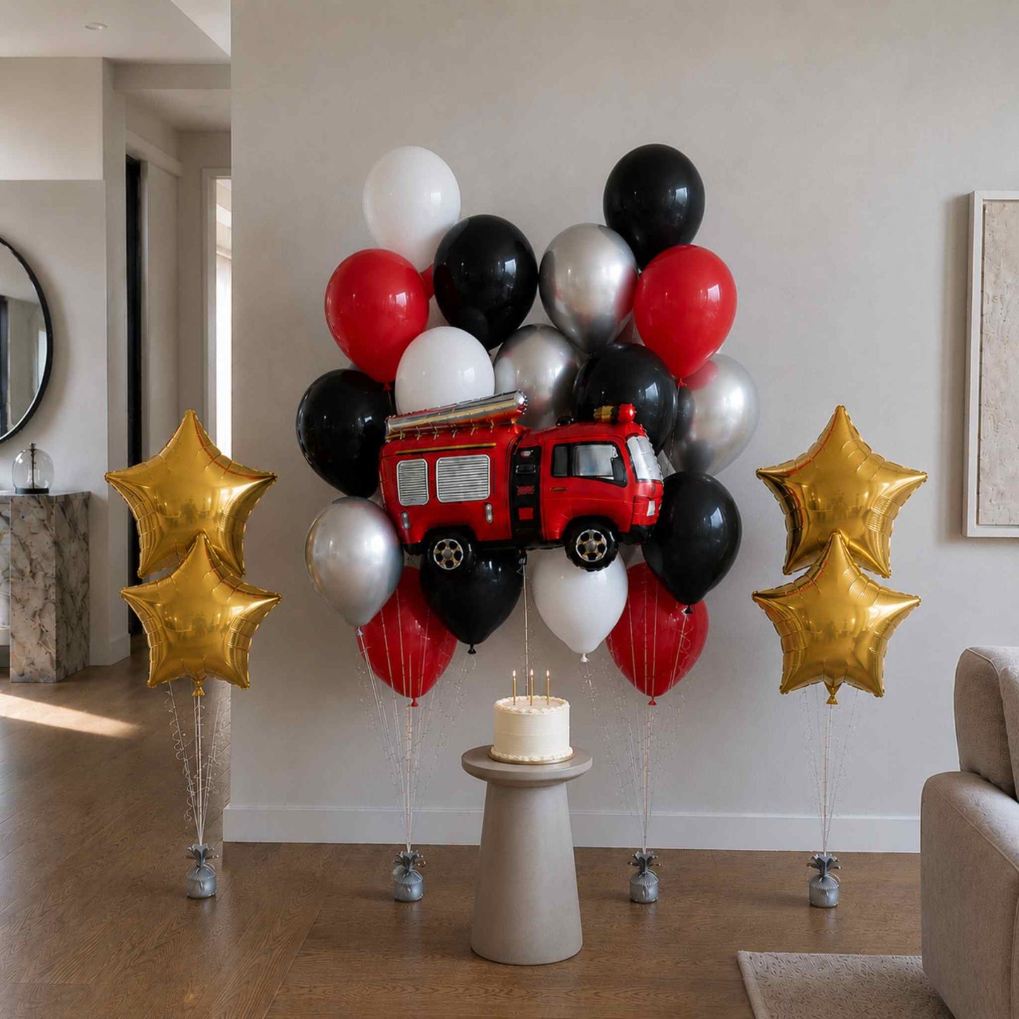 Balloon arrangement with a fire truck design and a cake on a pedestal in a room.