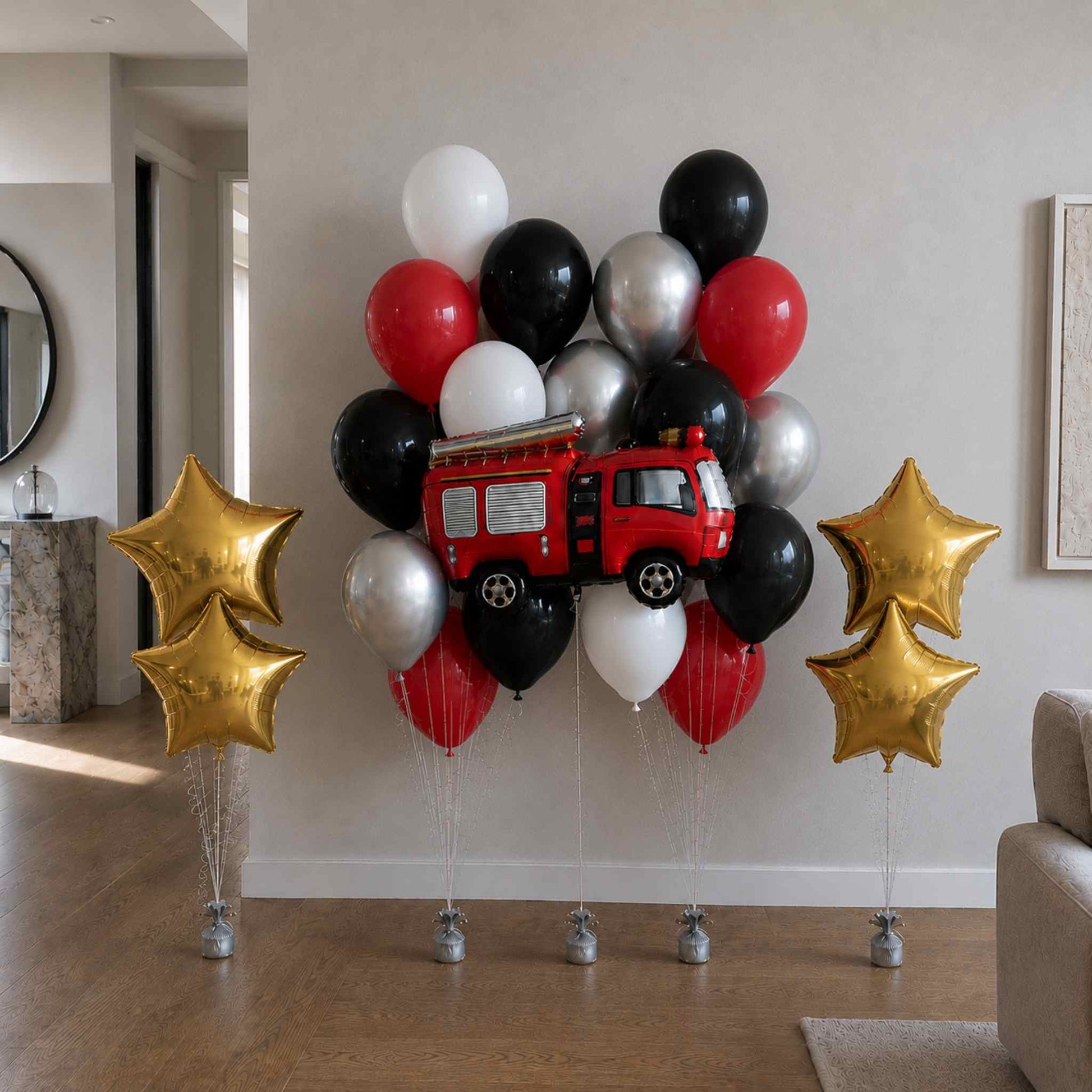 Balloon arrangement with a red fire truck toy, black, white, and gold balloons in a living room setting.