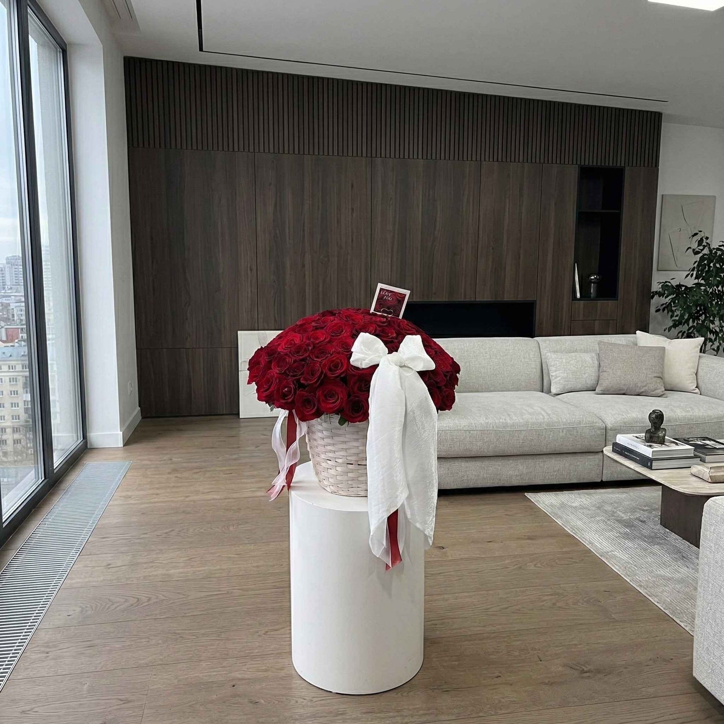 Modern living room with a vase of red flowers on a white pedestal.