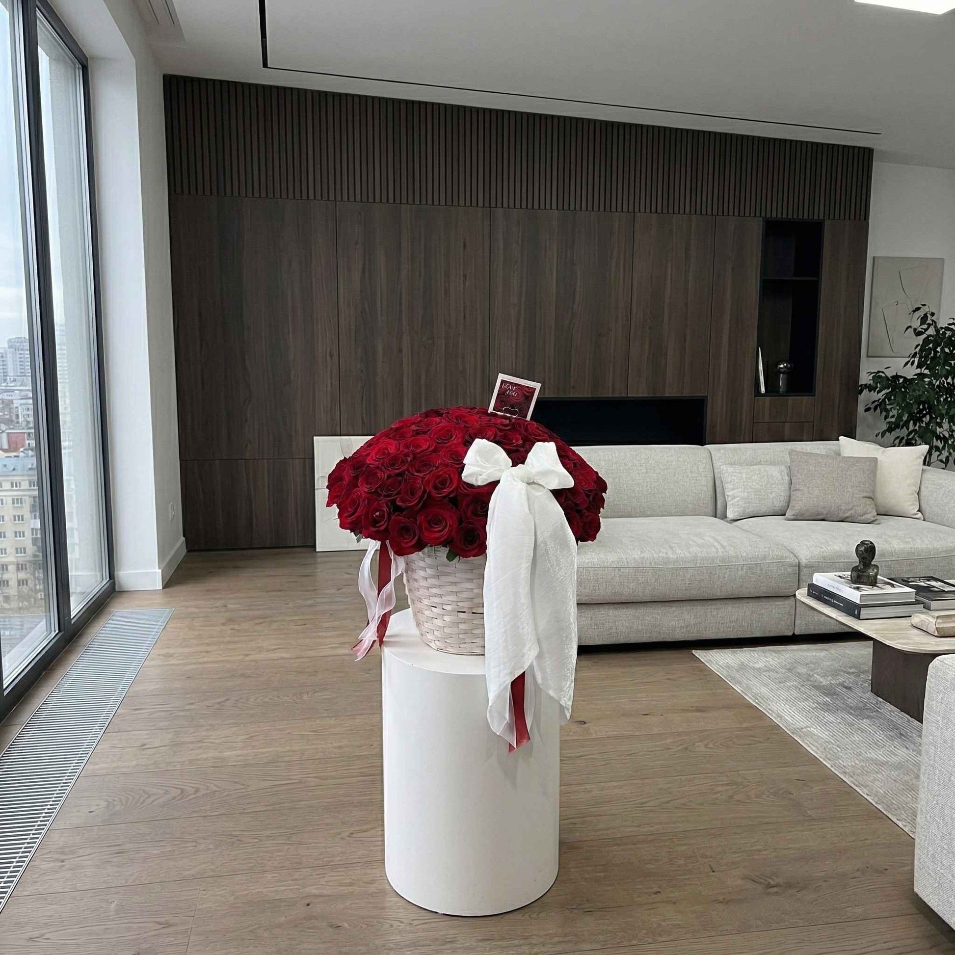 Modern living room with a vase of red flowers on a white pedestal.