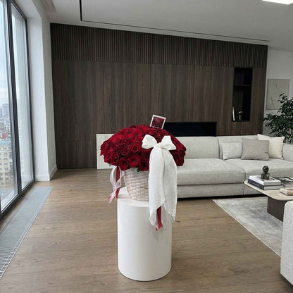 Modern living room with a vase of red flowers on a white pedestal.