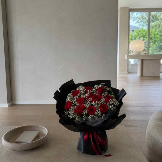 Bouquet of red roses wrapped in black paper with a red ribbon on a light wooden floor.