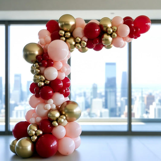 Balloon arch with red, pink, and gold balloons in front of a cityscape.