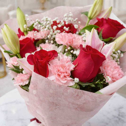 Bouquet of red roses and pink carnations wrapped in pink paper on a marble surface.