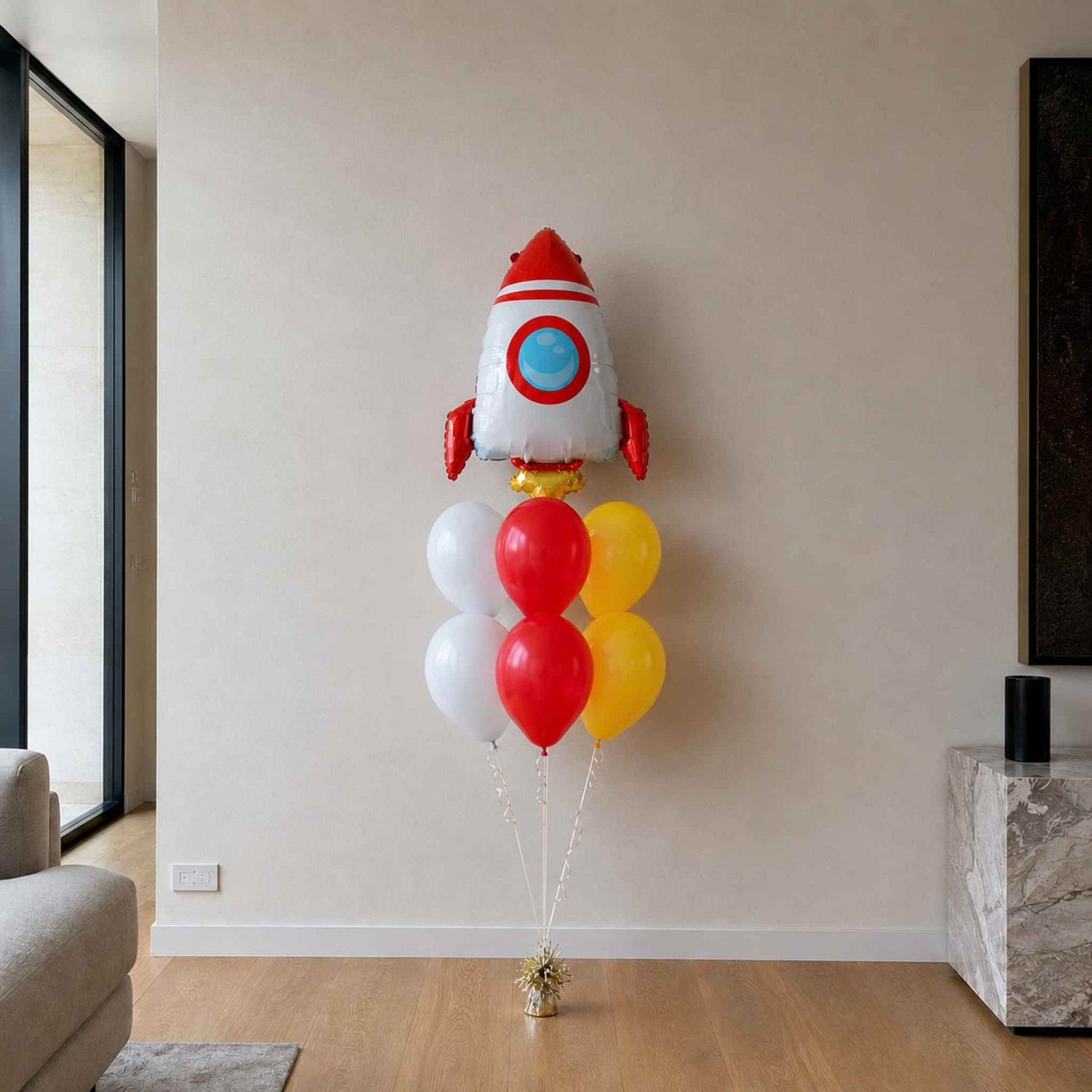Balloon arrangement shaped like a rocket with red, white, and yellow colors in a room.