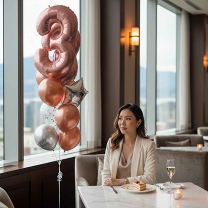 Woman sitting at a table with a cake and balloons in a room with large windows.