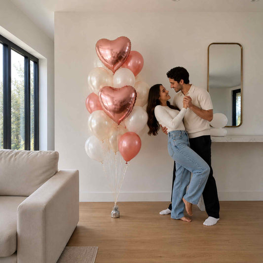 A couple embracing in a bright living room next to a cluster of metallic rose gold and white heart-shaped balloons.