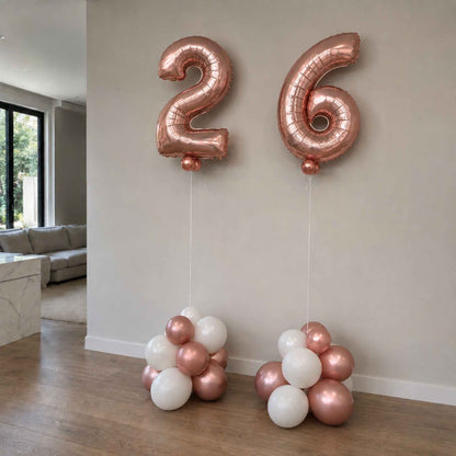 Rose gold and white number balloons spelling '26' in a living room setting.