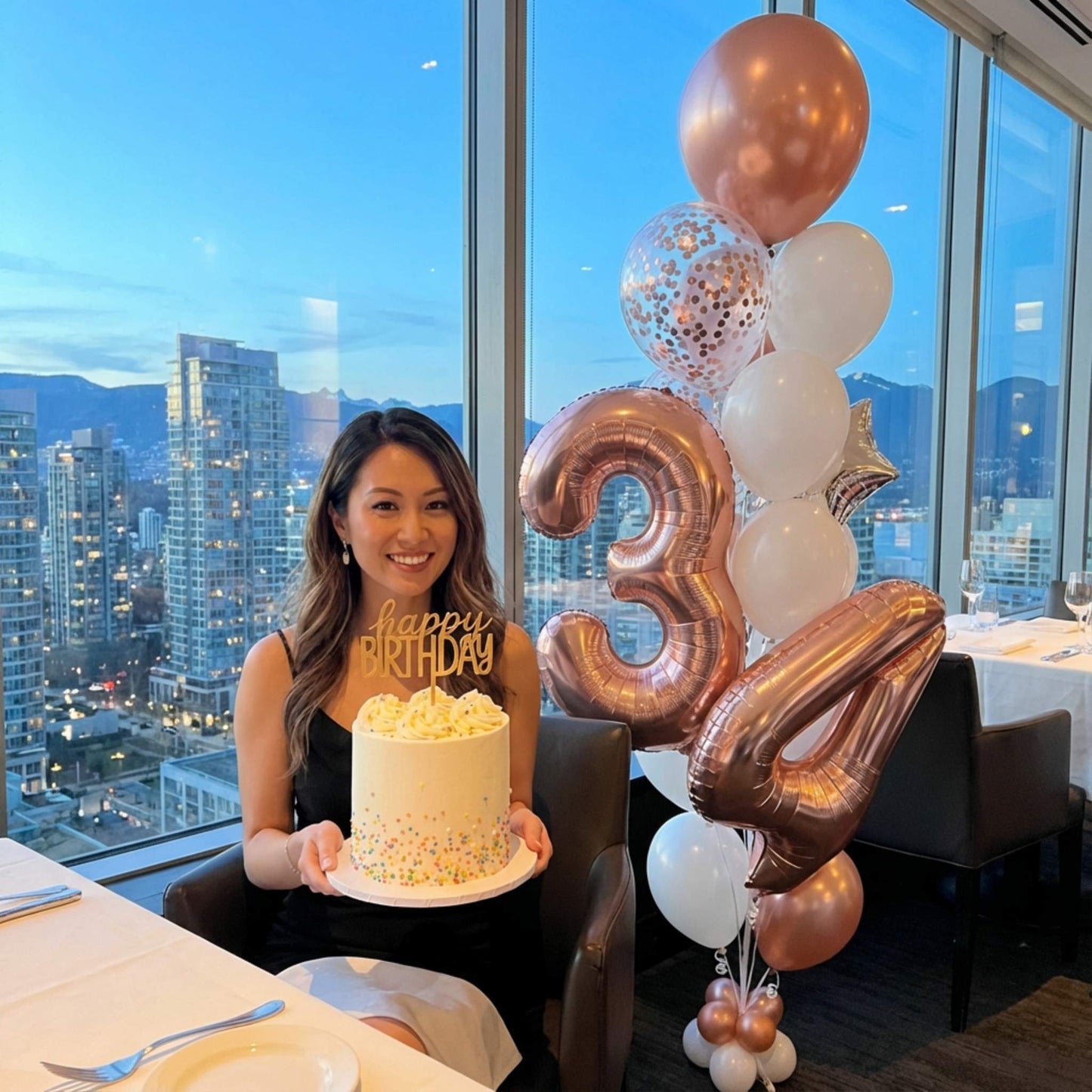 Woman holding a birthday cake with decorative balloons in a cityscape setting