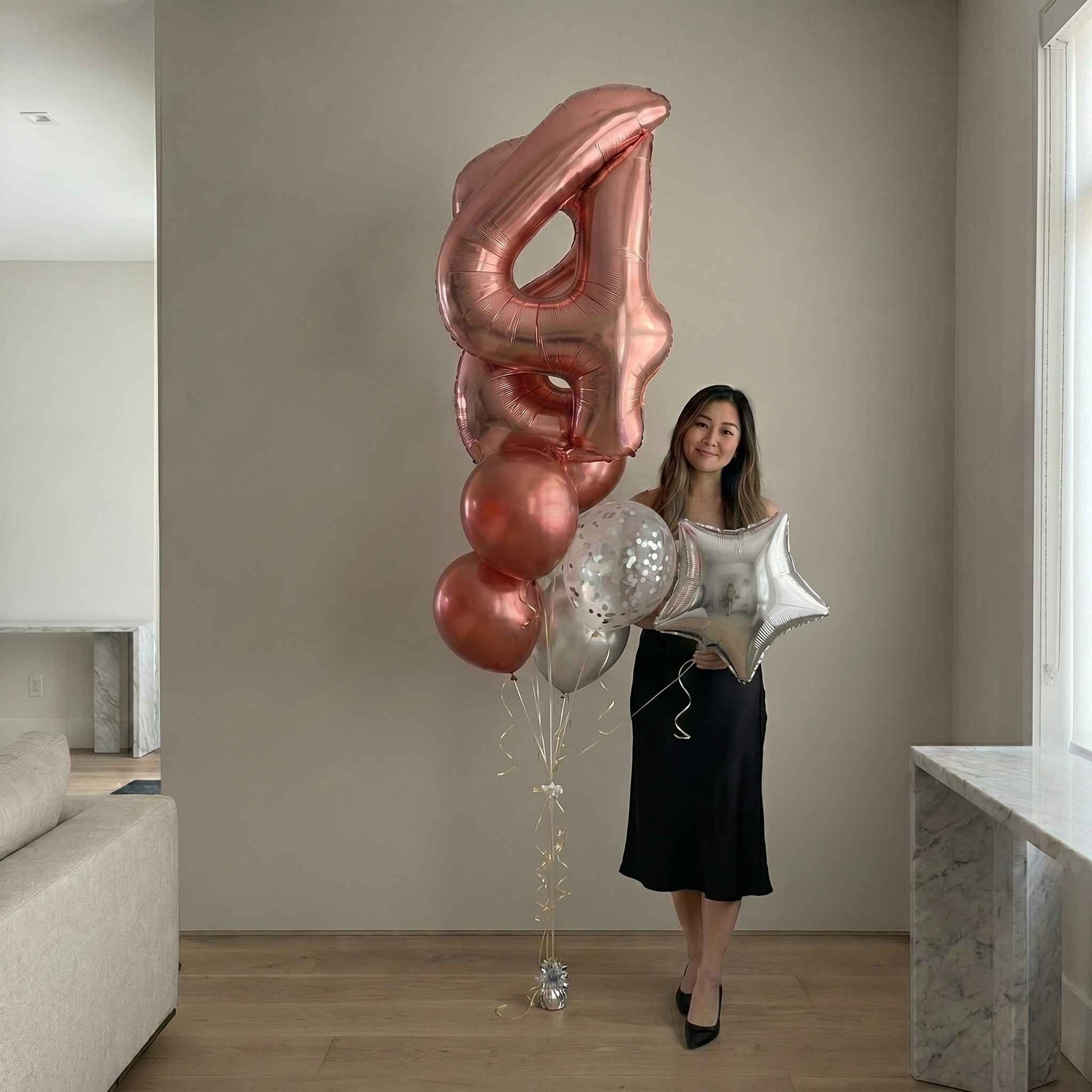 Woman holding a large number '4' balloon in a modern living room.