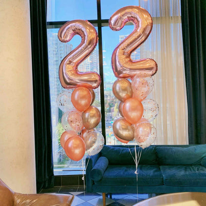 Rose gold number balloons '22' in a living room setting with a blue sofa and large window.