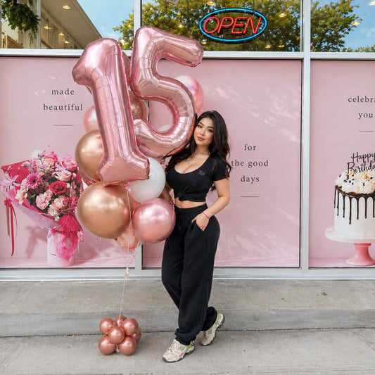 Person holding large pink number 15 balloons in front of a store window with decorative elements.