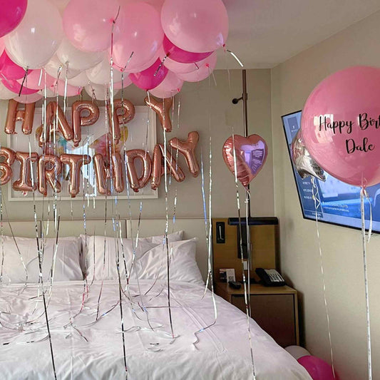 Bedroom decorated with pink balloons and 'Happy Birthday' sign, with a TV in the background.