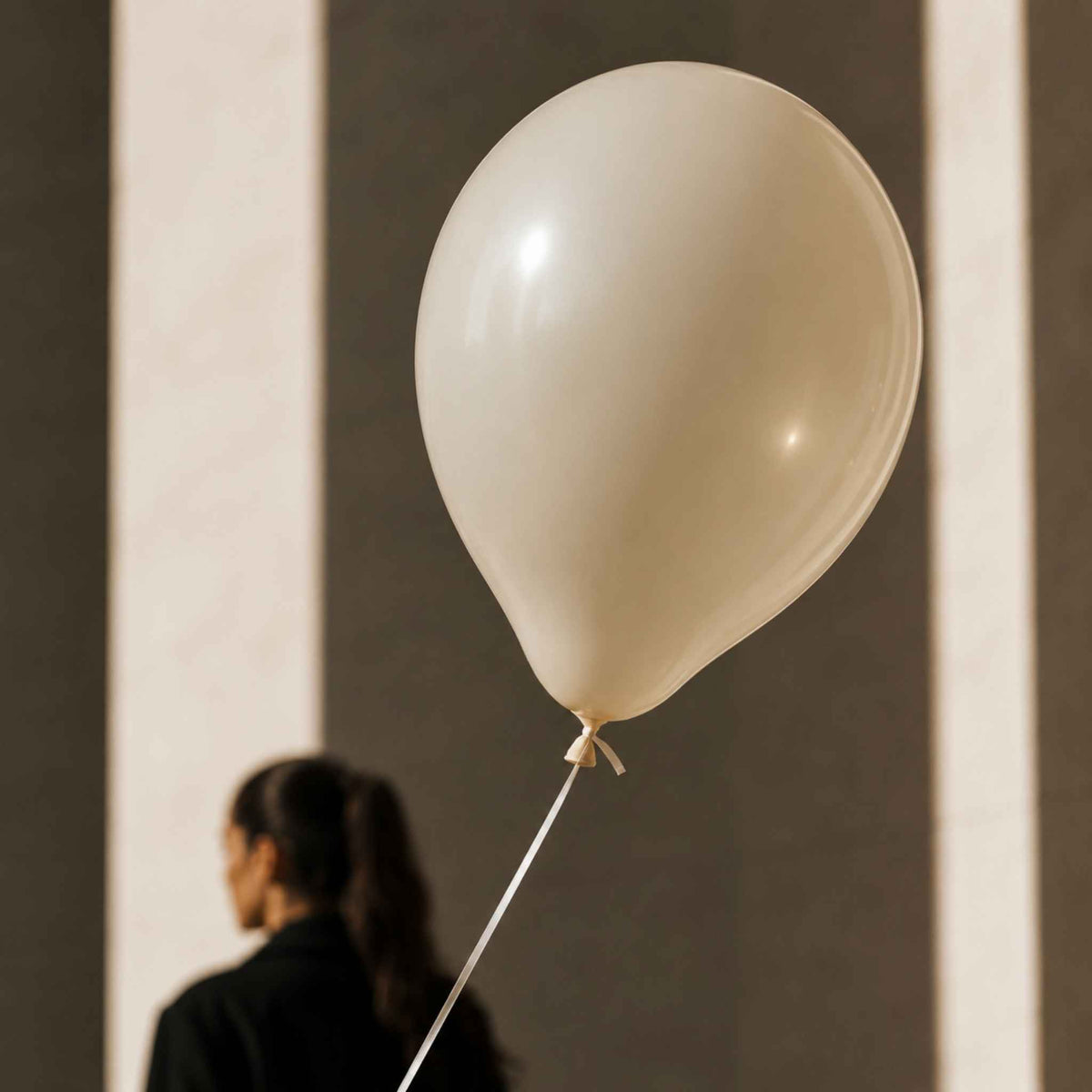 A large cream-colored latex balloon floating in front of a blurred background with a person visible from behind.