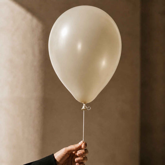 A single matte off-white balloon held by a hand against a warm beige textured wall.