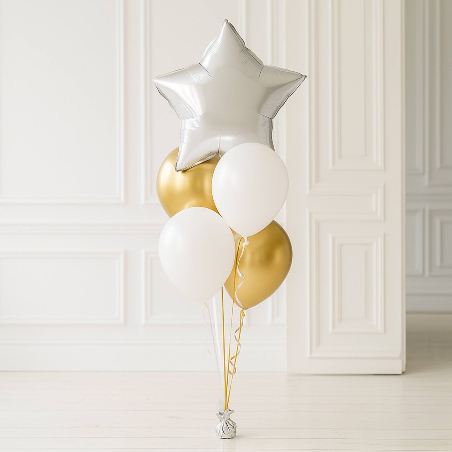 Decorative balloons including a silver star, gold, and white balloons against a white paneled wall.