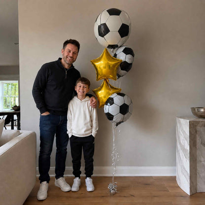 Man and child standing in a living room with soccer-themed balloons