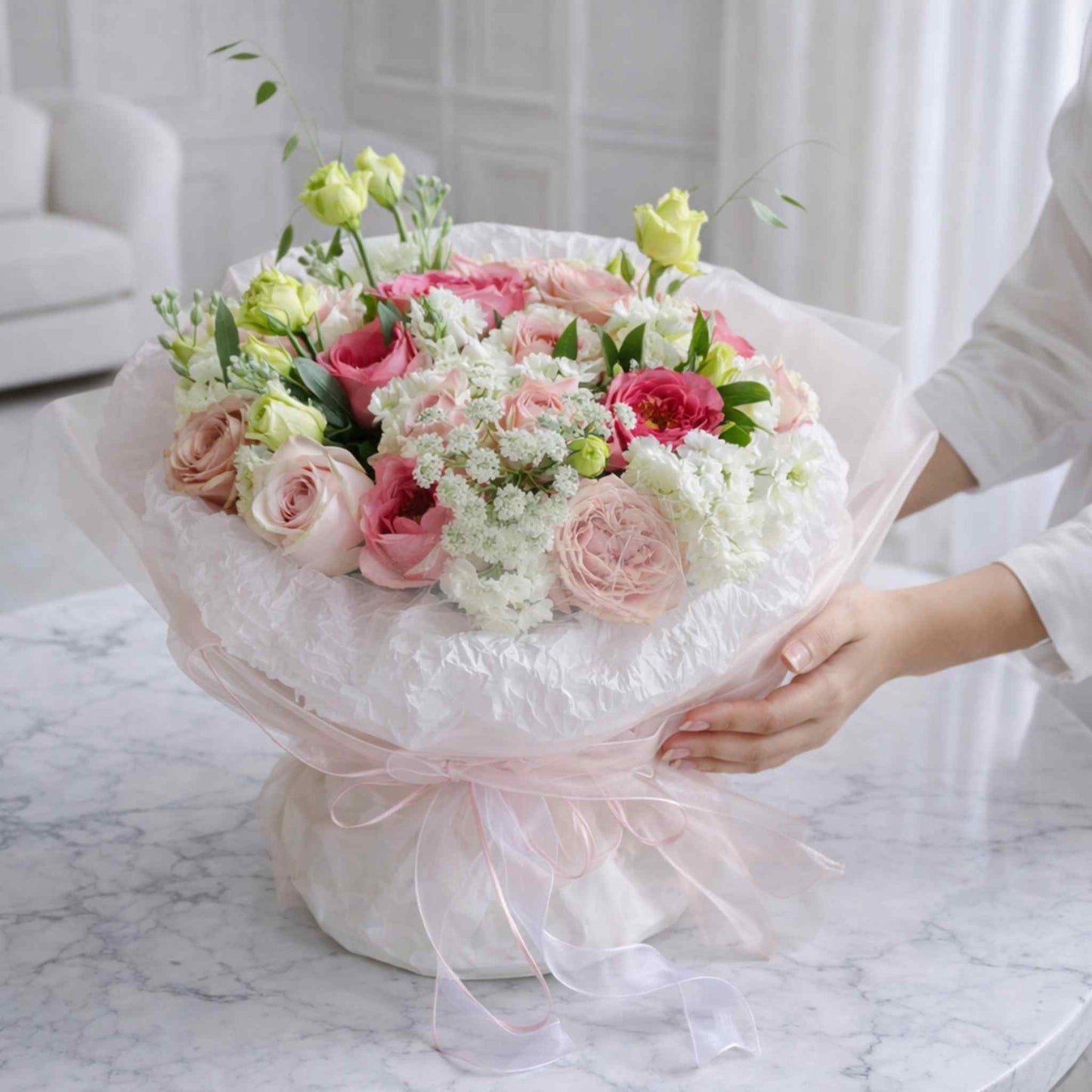 Bouquet of pink and white flowers with a person holding it indoors.