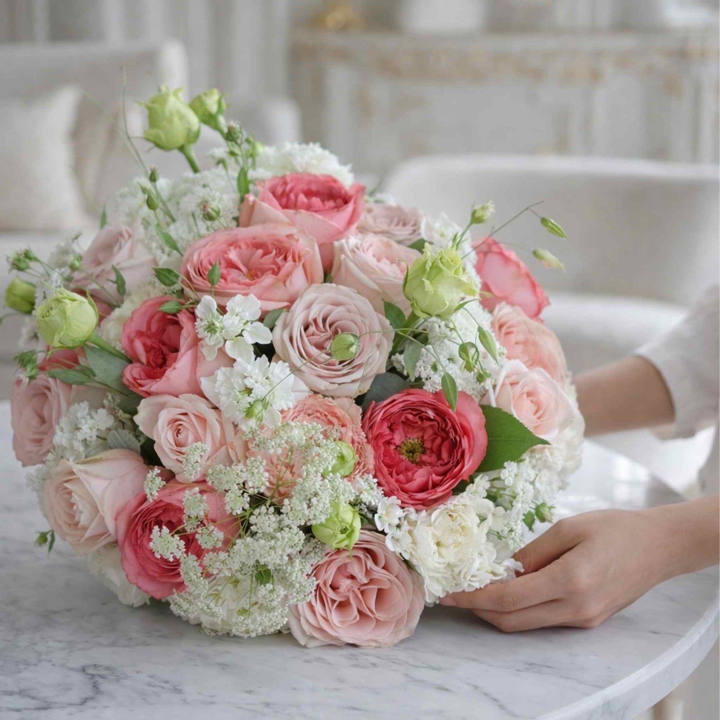Bouquet of pink and white flowers held by a person on a marble surface.