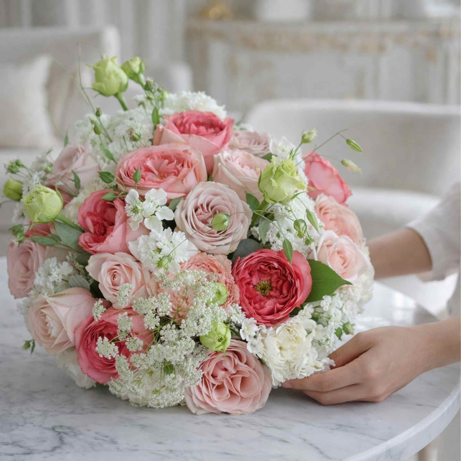 Bouquet of pink and white flowers held by a person on a marble surface.