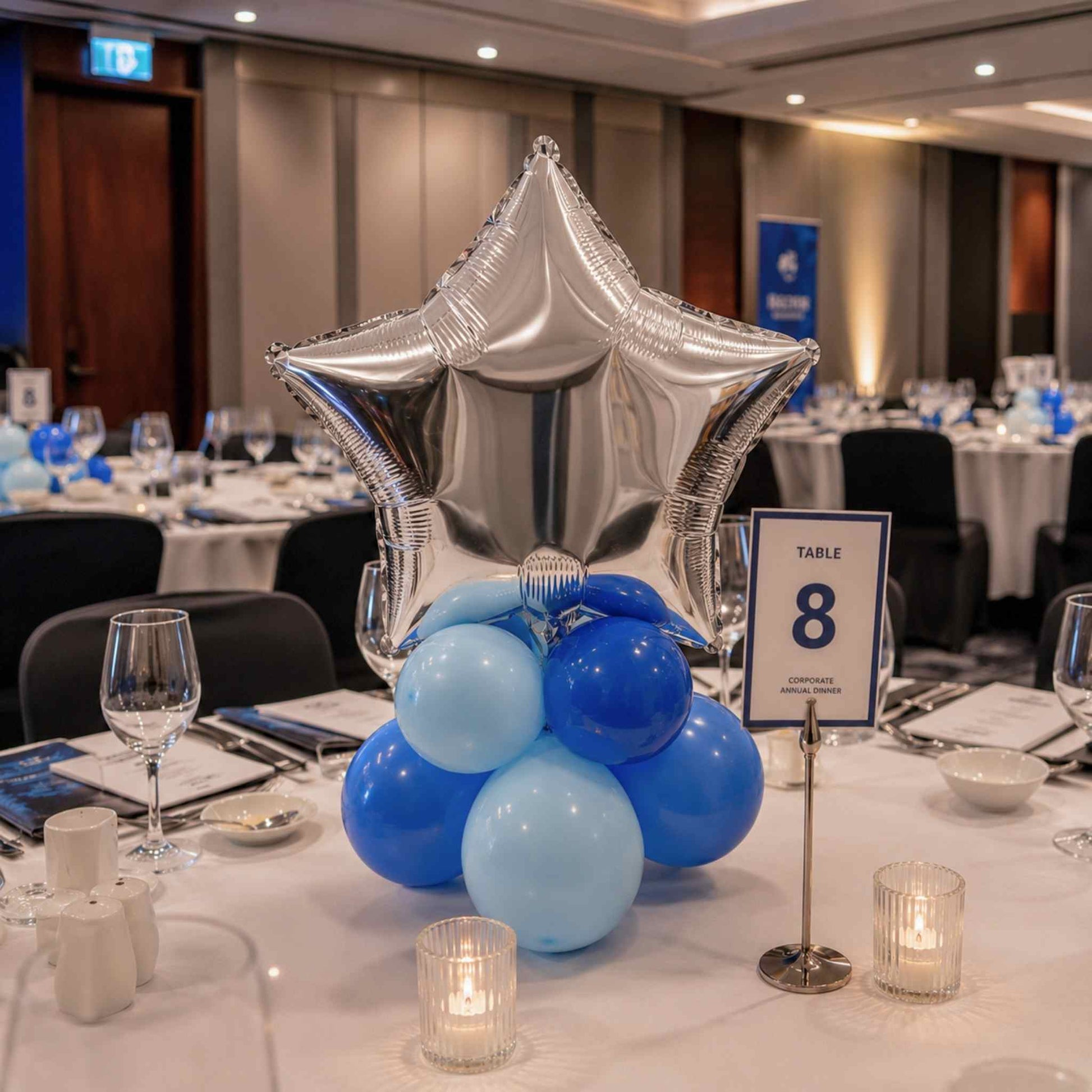 Decorative centerpiece with blue balloons and a silver star balloon on a table in a banquet hall.