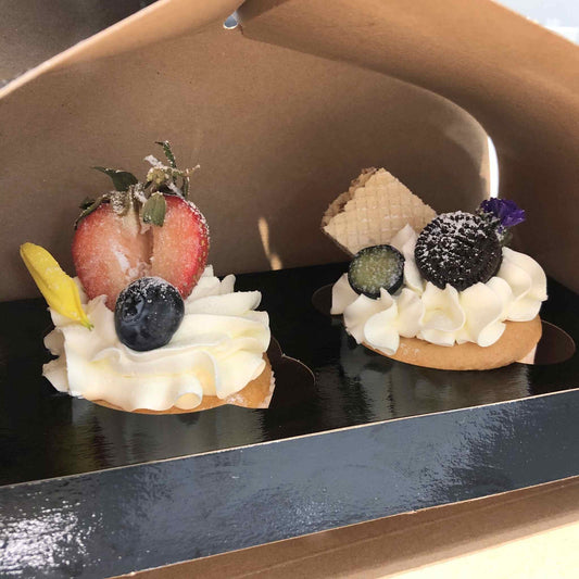 Two small desserts with whipped cream, berries, and a cookie on a black surface.