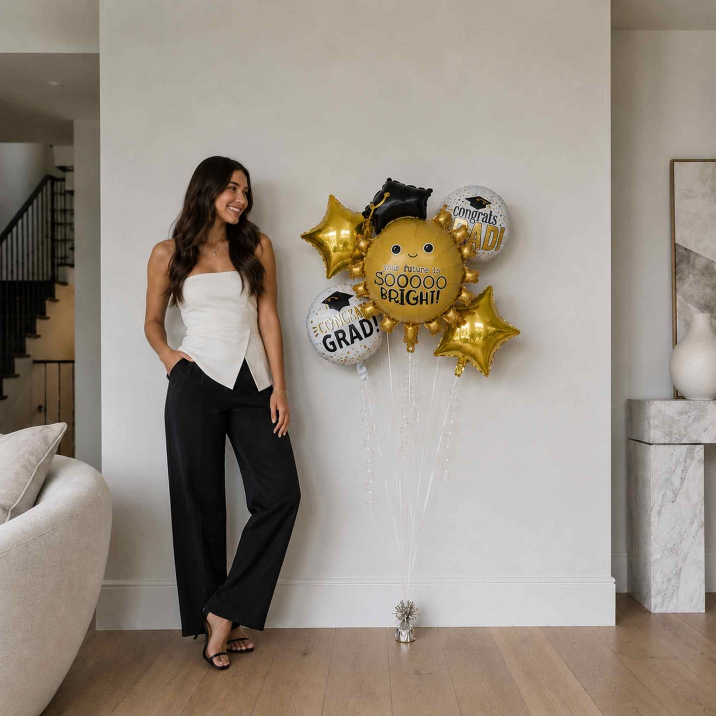 Woman standing next to a wall with graduation-themed balloons in a modern living room.