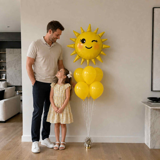 Man and young girl standing next to a large sun-shaped balloon in a living room.
