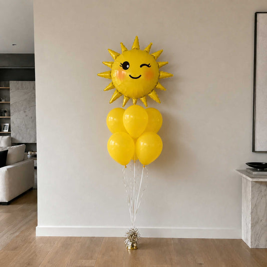 Yellow sun-shaped balloon with smiley face and attached balloons in a room.