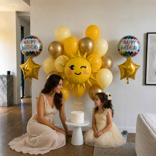 Two women with a birthday cake and sun-shaped balloon in a room.