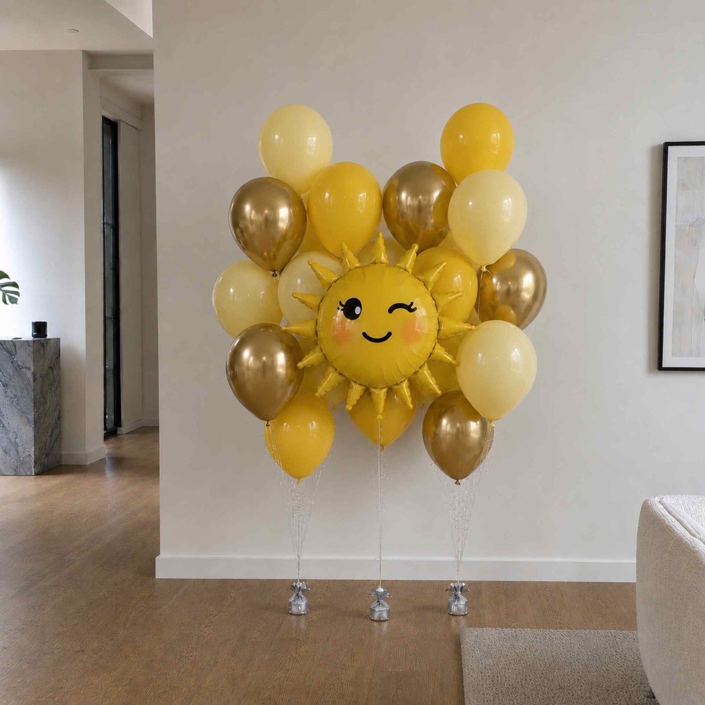 Sun-shaped balloon with smiley face surrounded by yellow and gold balloons in a room.